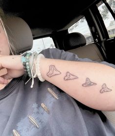 a woman sitting in the back seat of a car with tattoos on her arm and wrist