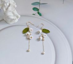 a pair of white flowers and leaves are hanging from earrings on a plate next to a statue