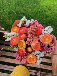 a bouquet of flowers sitting on top of a wooden bench next to a person's hand