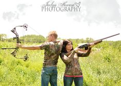 a man and woman are standing in the grass with their arms around each other while holding an arrow