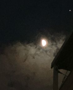 the moon is shining brightly in the night sky above some clouds and a house roof