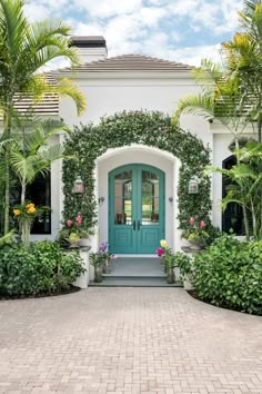 a blue door surrounded by greenery in front of a white house with palm trees