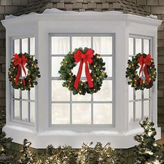 three christmas wreaths are hanging on the window sill in front of two evergreen trees