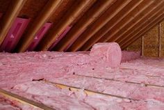 an attic with pink insulation and wood beams in the foreground, on top of wooden floor boards