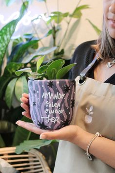 a woman holding a potted plant with writing on the side and saying, i am andy queen of tea