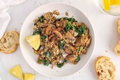 a white bowl filled with mushrooms and spinach next to slices of lemon wedges