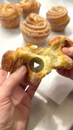 a person holding a pastry in front of some other pastries on a white surface