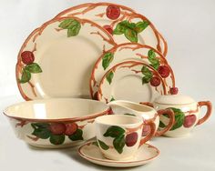 a set of porcelain dishes and cups with fruit designs on the rims are shown