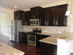 an empty kitchen with stainless steel appliances and granite counter tops, dark wood cabinetry