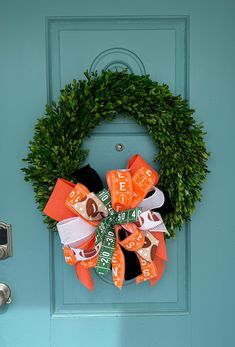 an orange and black football wreath on a blue front door with shoes hanging from it