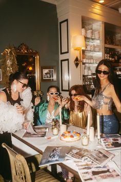 four women sitting at a table with cake and drinks in front of them, all wearing sunglasses