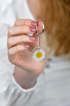 a woman holding a keychain with a flower on it's center and a ring around her thumb