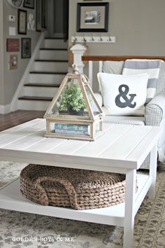 a white coffee table with a basket underneath it and some pictures on the wall behind it