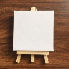 a wooden easel with a white canvas on it's legs sitting on a wood surface