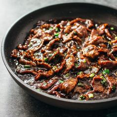 a black plate topped with meat covered in sauce and garnished with green onions