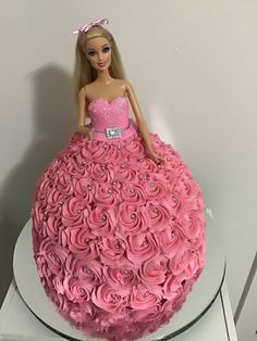 a barbie doll cake with pink frosting and roses on the top, sitting on a white plate