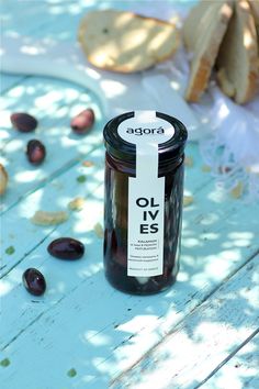 an open jar of olives sitting on top of a wooden table next to bread