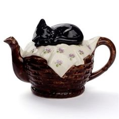 a ceramic teapot with a black cat sleeping on it's back in a basket