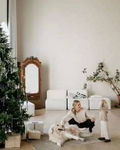 a woman sitting on the floor with her dog next to a christmas tree and presents