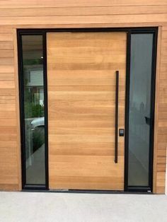 a modern wooden door with glass panels and black handles on the outside of a house