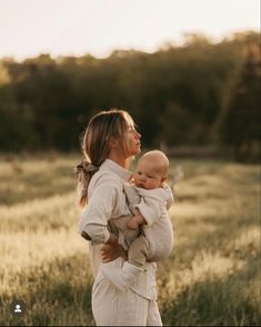 a woman holding a baby in her arms while standing in a field with tall grass