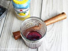 a glass filled with liquid sitting on top of a table next to a wooden spoon