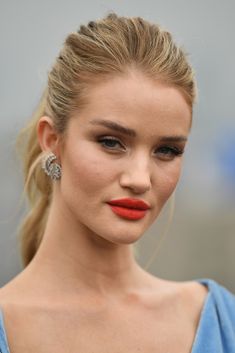 a close up of a woman with red lipstick and hair in a ponytail wearing earrings