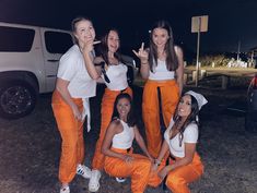 four girls in orange pants posing for the camera with their fingers up and one girl making peace sign