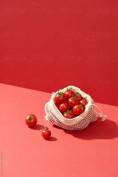 a bag full of tomatoes sitting on top of a pink surface next to two small red tomatoes