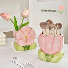 two vases filled with makeup brushes sitting on top of a table next to each other