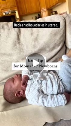 a baby laying on top of a white couch next to a wooden table and cabinets