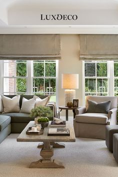 a living room with couches, chairs and tables in front of two large windows