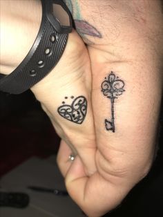 two people holding hands with tattoos on their fingers and one has a key in the middle