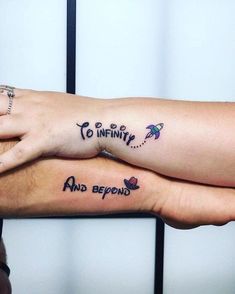 two people with matching tattoos on their arms holding each other's hands and saying to infinity and beyond