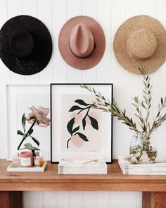 three hats are hanging on the wall above a wooden table with books and vases