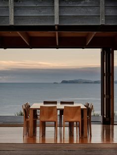 a table and chairs sitting on top of a wooden floor next to the ocean with an island in the distance