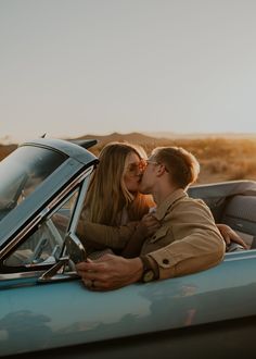 a man and woman kissing in the back of a blue car on a desert road