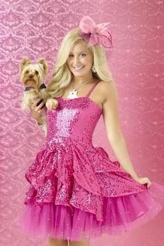 a woman in a pink dress holding a dog and posing for the camera with her hand on her hip