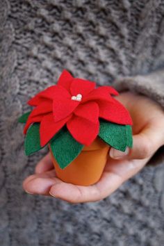 a hand holding a small plastic flower in it's left hand, with felt flowers on the top