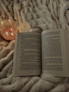 an open book sitting on top of a bed next to a candle