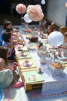 a group of children sitting around a table with food on it and balloons in the air