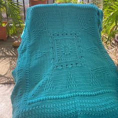 a blue crocheted blanket sitting on top of a wooden table next to a potted plant