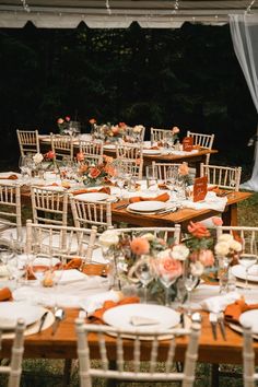 an outdoor wedding reception with white chairs and orange napkins set up for the table