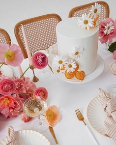 the table is set with pink and white flowers, gold cutlery, and a wedding cake