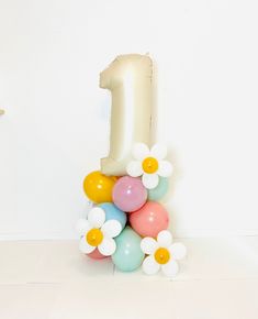 the number one balloon is surrounded by balloons and daisies in front of a white wall