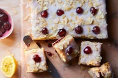 a cutting board topped with slices of cake next to a bowl of fruit and a knife