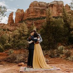 a man and woman standing next to each other on a blanket in front of mountains