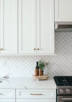 white kitchen with herring tile backsplash and brass pulls on the cabinet doors,