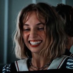 a smiling woman with blonde hair wearing a striped shirt and silver necklace, looking at her laptop screen