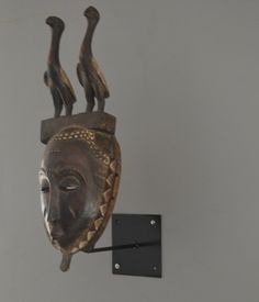 a wooden mask hanging on the wall next to a black hook with two birds perched on it